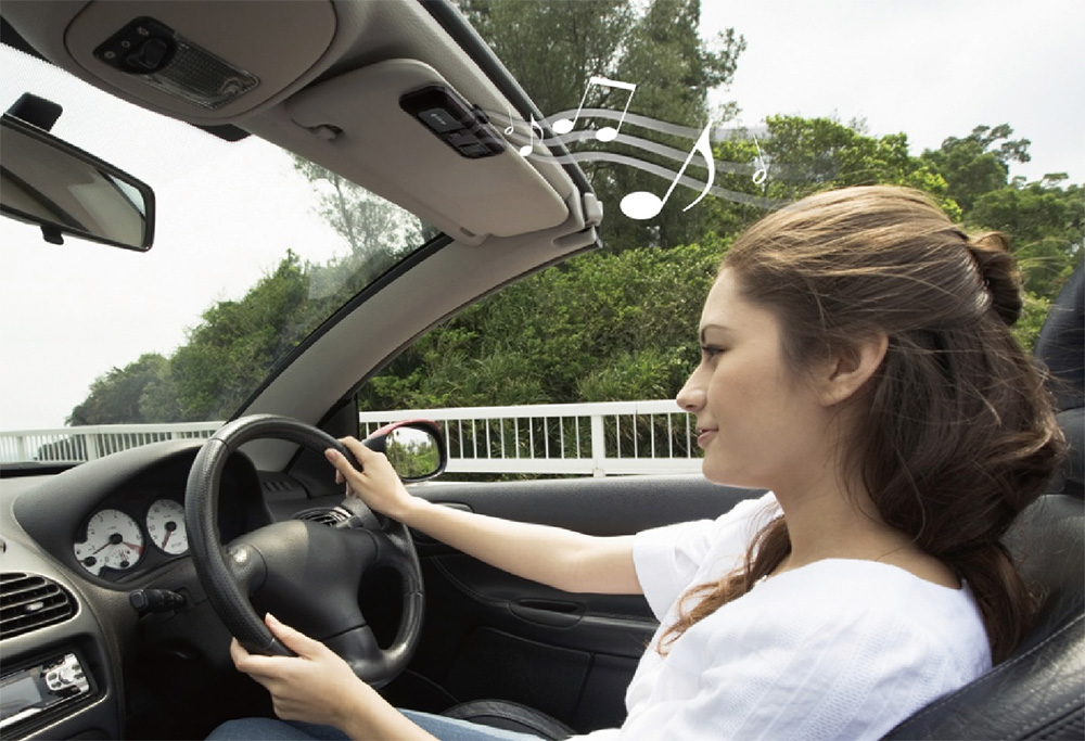 CK-01 CARKIT 2 Image of a girl driving while using a speakerphone clipped to the sun visor, demonstrating a hands-free setup for safe and convenient in-car conversations